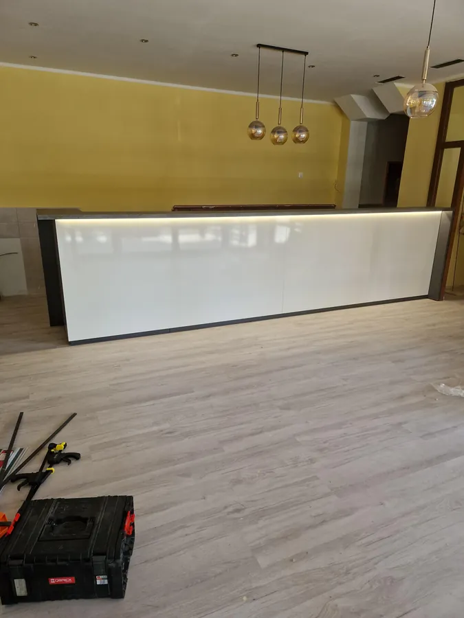 Dlhý recepčný pult s bielym podsvieteným čelným panelom a tmavým rámom